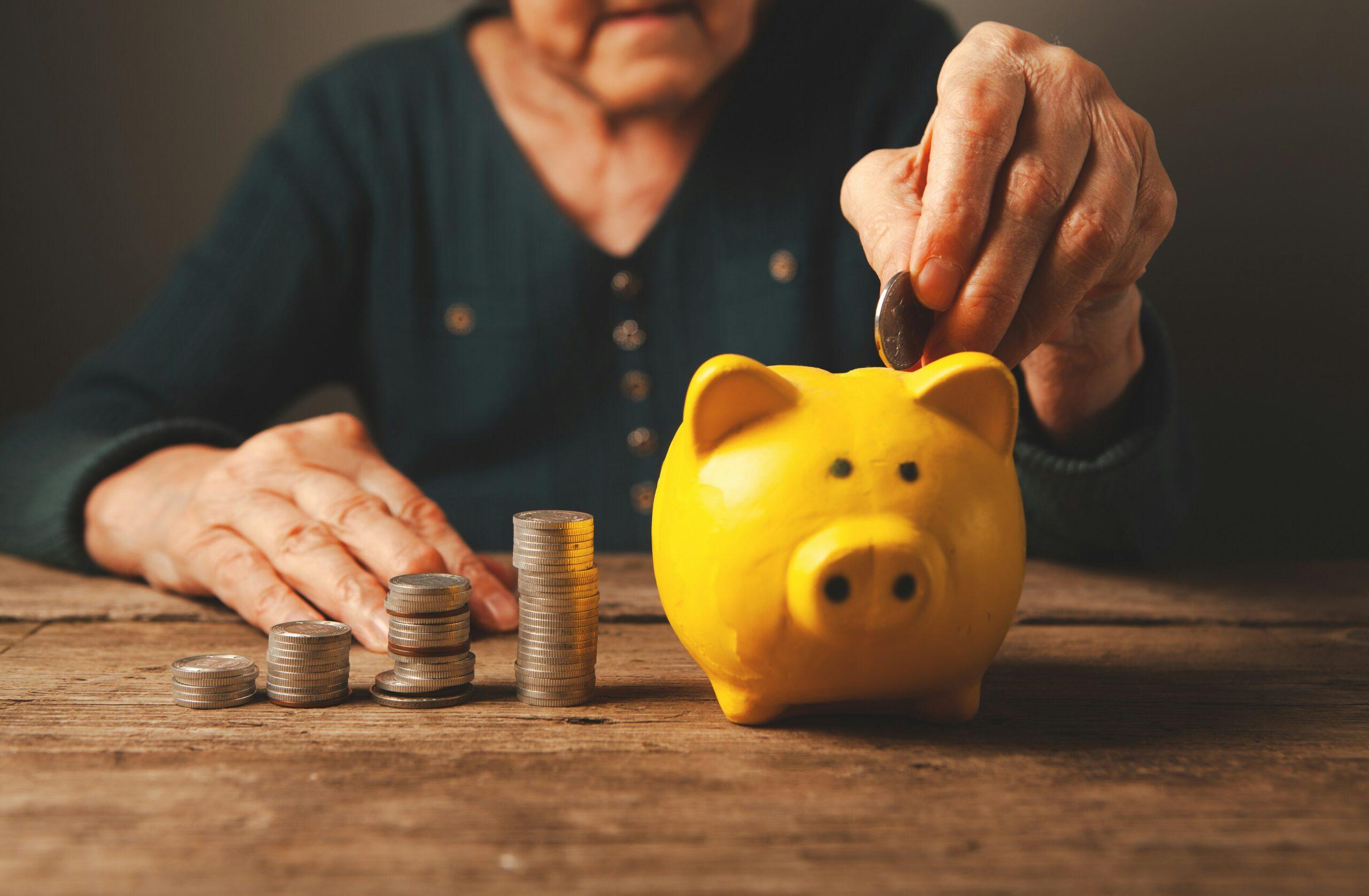 sasun-bughdaryan-z3TnzxotdPc-unsplash Elderly person depositing coins into a yellow piggy bank.